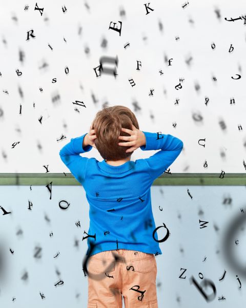 Un enfant fixant un mur, se tenant la tête entre les mains, se trouve au milieu d'une avalanche de lettres