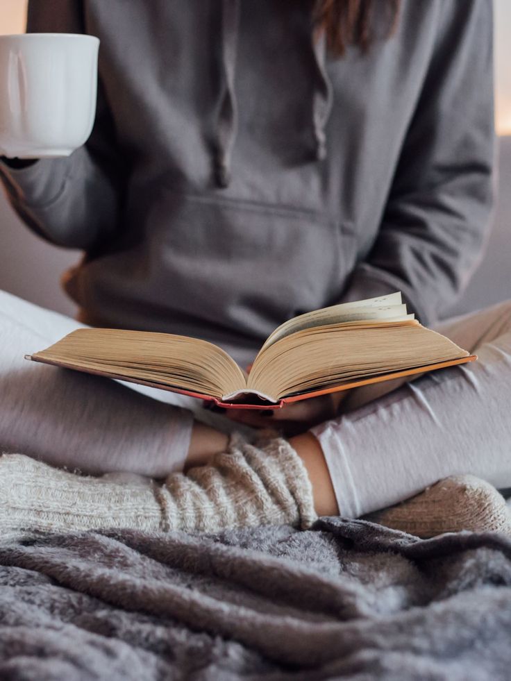 Une lectrice, confortablement assise en tailleur sur un canapé, 
                    tasse de café à la main, est en train de lire